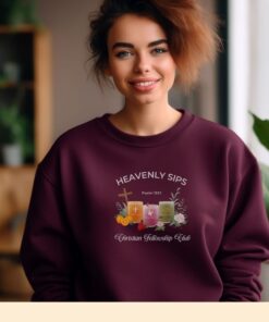 Maroon sweatshirt with Three faith-inspired juice glasses: Joyful Juice (orange with a cross), Blessed Berry (pink with a dove), and Graceful Green (green with a fish).