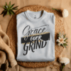 Ash Colored Gildan 5000 Grace Over Grind t-shirt features bold calligraphy, gold and black brushstrokes, and an inspirational Christian faith message
