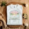 White Flat fold Children Are a Gift From God Floral Christian T-Shirt featuring a watercolor sunrise, handprint flowers, and faith-based quote.
