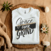 White Gildan 5000 Grace Over Grind t-shirt features bold calligraphy, gold and black brushstrokes, and an inspirational Christian faith message